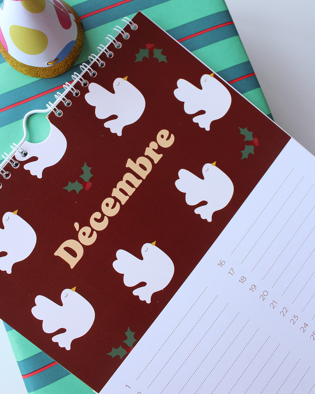 Une page du "Calendrier des anniversaires" de Ma Petite Vie pour le mois de décembre présente des colombes blanches, des feuilles de houx vertes et "Décembre" en or sur fond bordeaux. Un cadeau familial idéal.